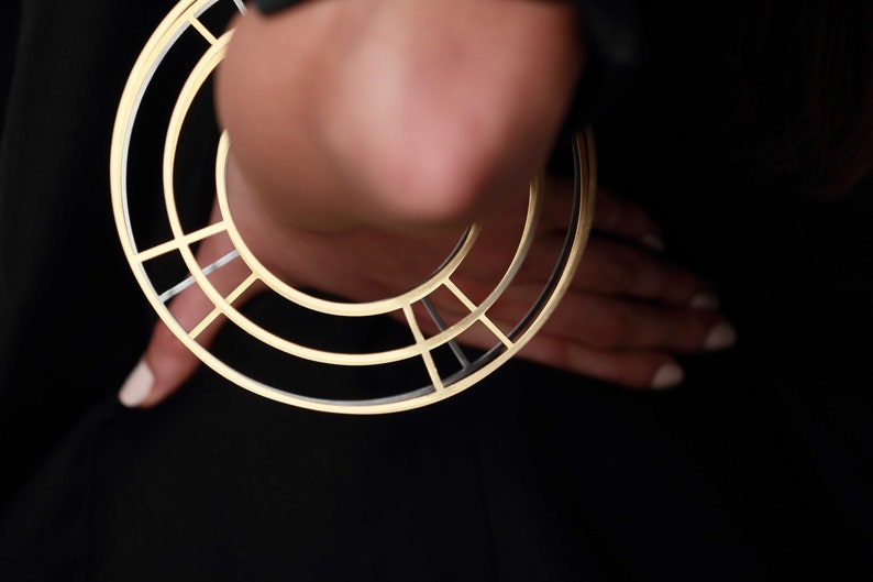 Puede incluir: Un aro de oreja geom&eacute;trico de oro y plata con un dise&ntilde;o circular.