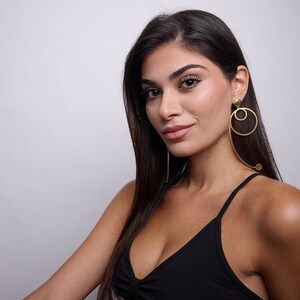 May include: A woman with long dark hair wearing a black tank top and large gold hoop earrings.