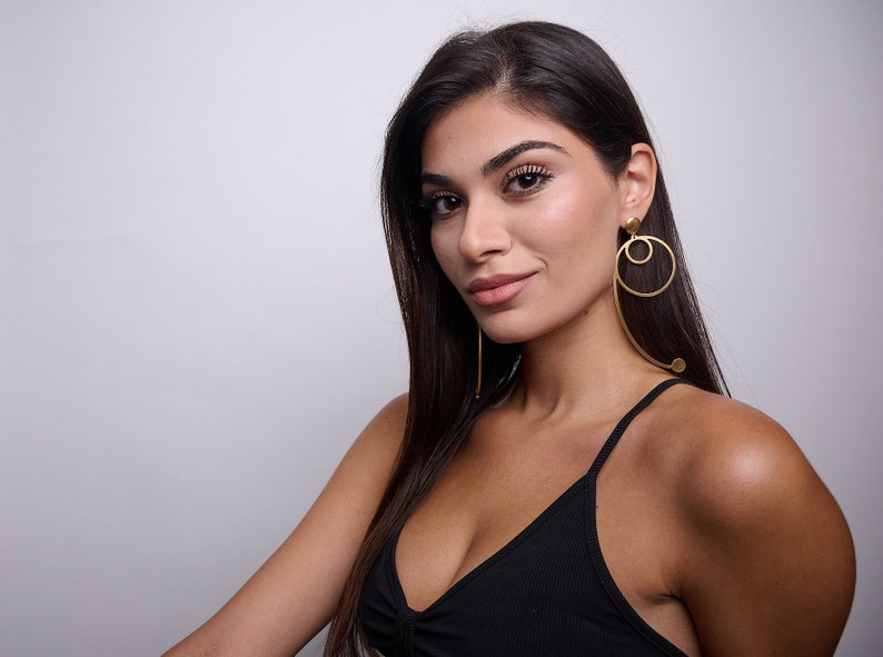 May include: A woman with long dark hair wearing a black tank top and large gold hoop earrings.