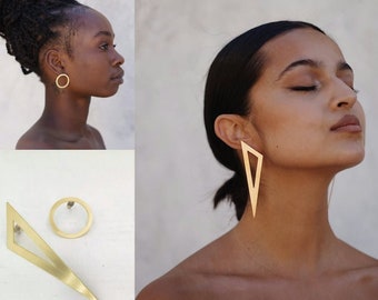 May include: A pair of gold-toned earrings consisting of one circular stud and one elongated triangular drop earring. The circular earring is a simple hoop, while the triangular earring features a hollow center and a pointed, geometric design.