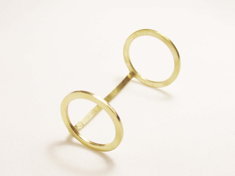 May include: A gold-coloured metal bracelet with two circular openings. The bracelet is made from a single piece of metal that is bent into a loop shape.