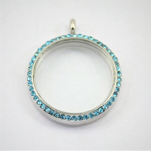 May include: Silver locket pendant with a round, clear glass insert and a border of light blue rhinestones.