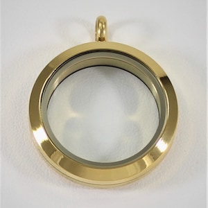 May include: Gold-toned locket pendant with a clear glass insert. The locket has a simple design and is perfect for adding a personal touch to any jewelry collection.