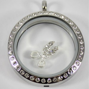 May include: Silver locket necklace with a clear glass insert and a silver charm of a pair of scissors with clear rhinestones. The locket is surrounded by a row of clear rhinestones.