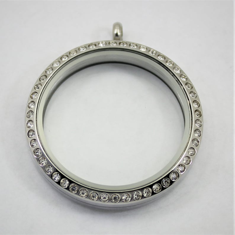 May include: A silver locket with a clear glass insert and a circle of clear rhinestones around the edge.