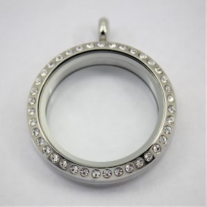 May include: Silver locket pendant with a clear glass insert and a border of clear rhinestones.