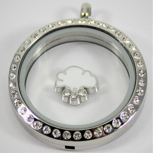 May include: A silver locket necklace with a clear glass insert and a white cloud charm with clear crystal accents. The locket is surrounded by a row of clear crystals.