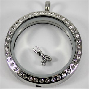 May include: A silver locket with a clear glass insert and a silver charm of a pair of scissors. The locket is surrounded by a row of clear rhinestones.
