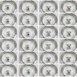 May include: A set of 20 silver locket charms featuring a variety of colorful gemstones. Each charm is a small figure of a person or a bear.