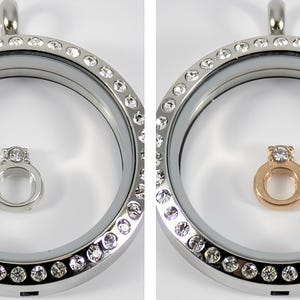 May include: Two silver locket necklaces with a clear glass insert. The locket on the left has a silver ring charm with a single clear stone. The locket on the right has a gold ring charm with a single clear stone.