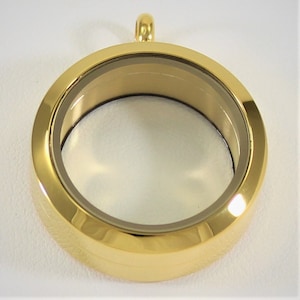 May include: Gold-toned round locket pendant with a clear glass insert. The locket has a smooth, polished finish.