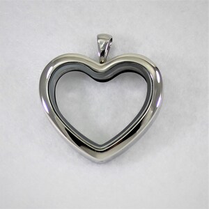 May include: A polished silver heart-shaped pendant. The pendant has a hollow center and a small loop at the top for a chain. The heart is smooth and reflective, with a simple, elegant design. The pendant is likely made of stainless steel.