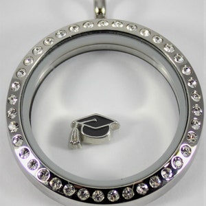 May include: Silver locket with a clear glass insert and a graduation cap charm. The locket is decorated with a row of clear crystals around the edge.