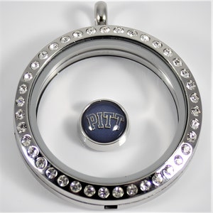 May include: Silver locket necklace with a clear glass insert and a blue and gold charm with the word "PITT" on it. The locket is surrounded by a row of clear rhinestones.