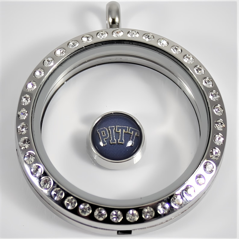 May include: Silver locket necklace with a clear glass insert and a blue and gold charm with the word "PITT" on it. The locket is surrounded by a row of clear rhinestones.