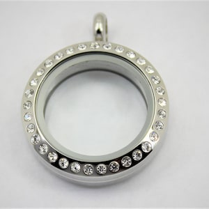 May include: A silver locket pendant with a clear glass insert and a circle of clear rhinestones around the edge.