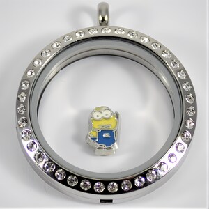 May include: A silver locket with a clear glass insert and a silver chain. The locket is decorated with a row of clear rhinestones around the edge. The locket contains a small yellow and blue cartoon character charm.