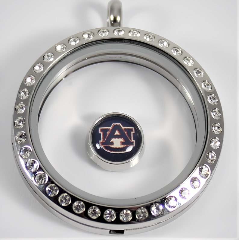May include: Silver locket necklace with a clear glass insert and a round charm with the Auburn University logo. The locket is decorated with clear rhinestones.