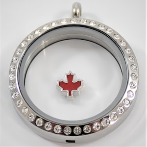 May include: Silver locket with a clear glass insert and a red maple leaf charm. The locket is surrounded by a row of clear crystals.