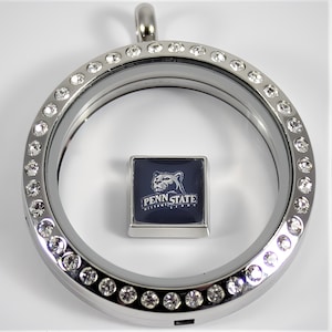 May include: Silver locket with a clear glass insert and a crystal-encrusted border. The locket contains a square charm with a blue background and a white image of a lion with the text "Penn State Nittany Lions".