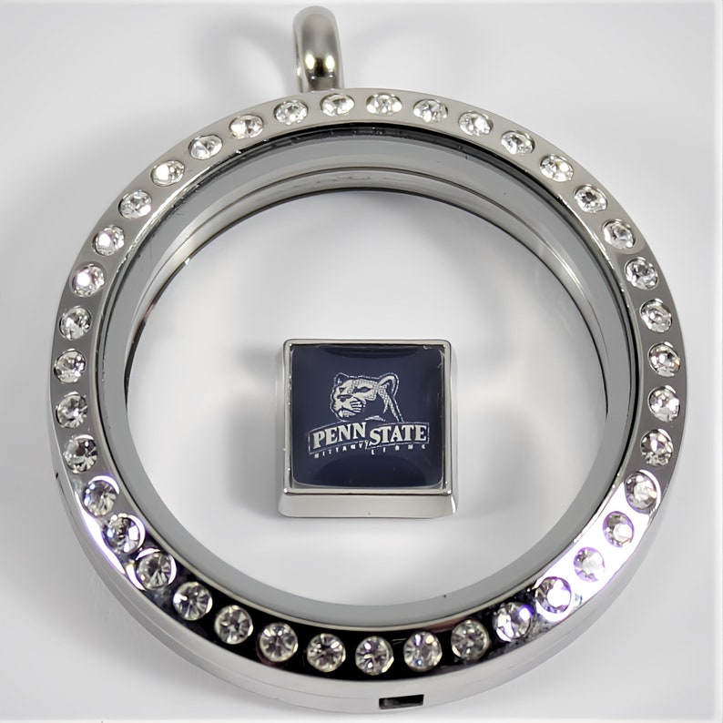 May include: Silver locket with a clear glass insert and a crystal-encrusted border. The locket contains a square charm with a blue background and a white image of a lion with the text "Penn State Nittany Lions".