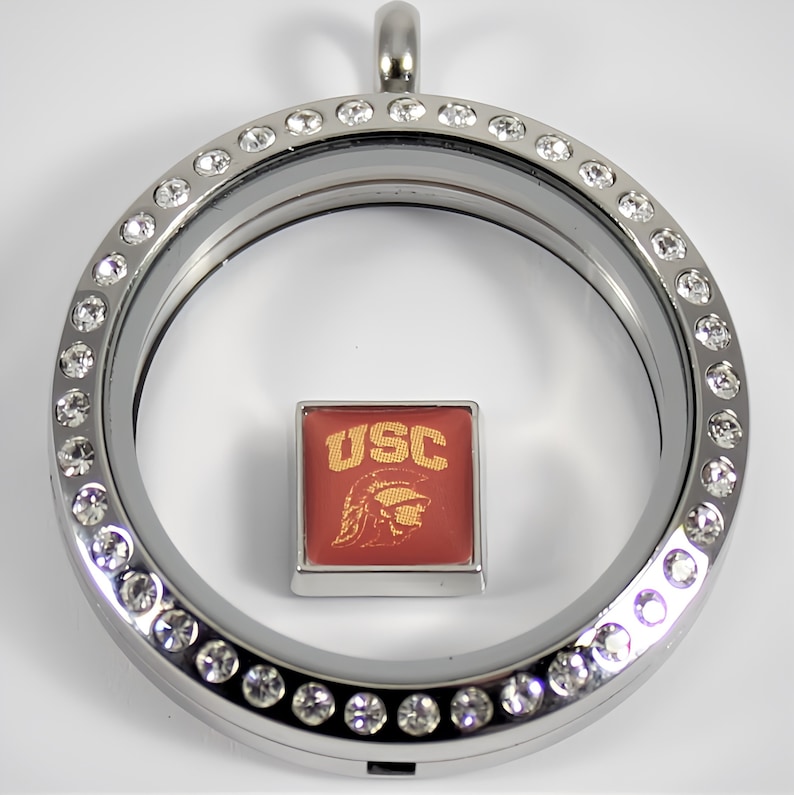 May include: Silver locket with a clear glass insert and a crystal-encrusted border. The locket contains a square charm with the letters "USC" in gold and a red and gold mascot image.