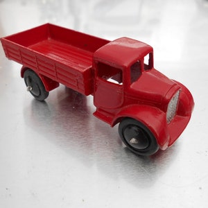 May include: A red toy truck with a flatbed and black wheels. The truck is made of metal and has a detailed design.