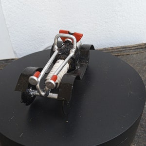 Può includere: Un'auto giocattolo nera e argentata realizzata con materiali riciclati. L'auto ha accenti rossi e un tubo di scarico bianco.