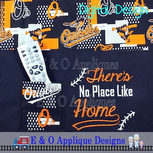 May include: A black fabric with an orange and white embroidered design that says "There's No Place Like Home" with a baseball theme. The fabric has a pocket with a white and orange embroidered design that says "Orioles".