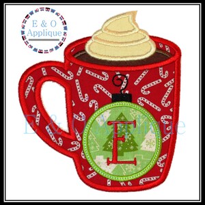 May include: Red and white candy cane patterned mug with whipped cream and chocolate on top. A green and white ornament with a letter E and a small Christmas tree is attached to the mug.