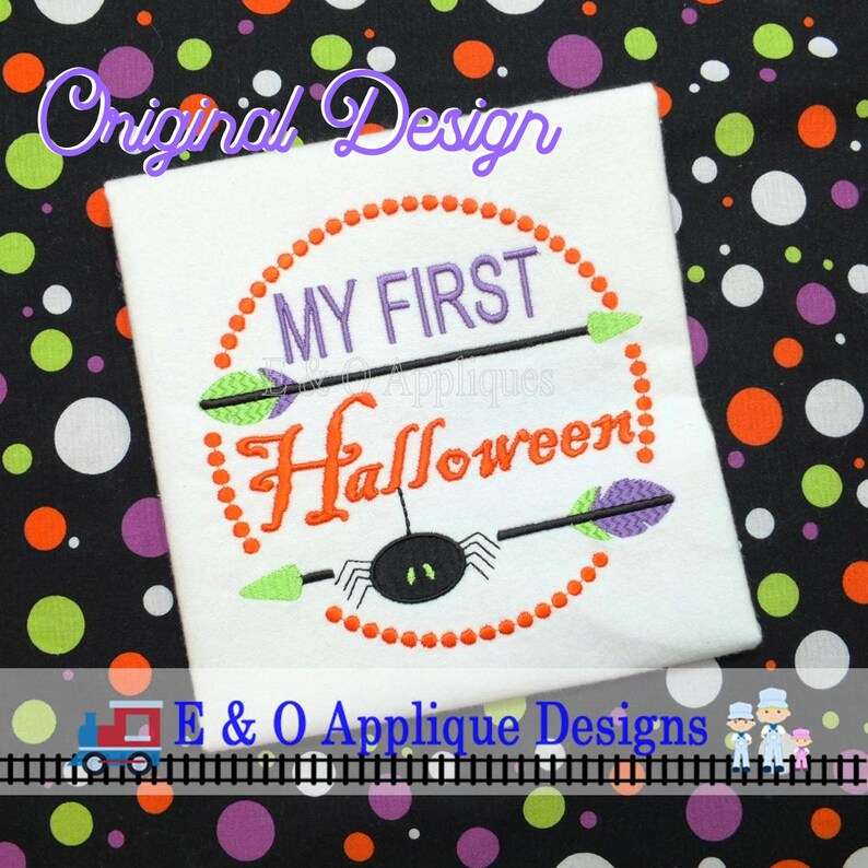 May include: White fabric with an orange, green, and purple embroidered design that says "My First Halloween" with a spider in the center. The design is surrounded by a circle of orange dots.
