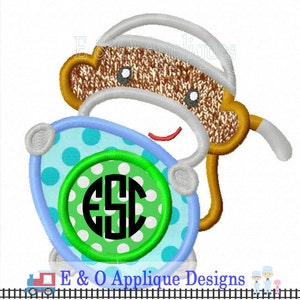 May include: A brown and gray monkey holding a blue and green circle with white polka dots. The circle has a black monogram in the center. The monkey is wearing a white hat.