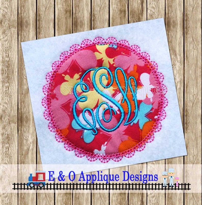 Puede incluir: Una aplicaci&oacute;n circular rosa y blanca con un monograma azul en el centro. El c&iacute;rculo tiene un borde festoneado rosa.