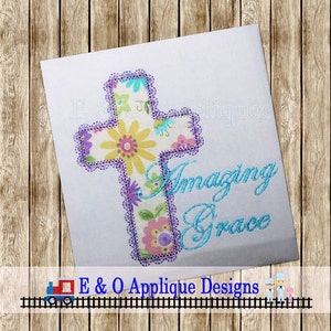 May include: A white square with a floral cross design. The cross is filled with a colorful floral pattern and outlined with purple lace. The words "Amazing Grace" are written in blue script. The design is by E & O Applique Designs.
