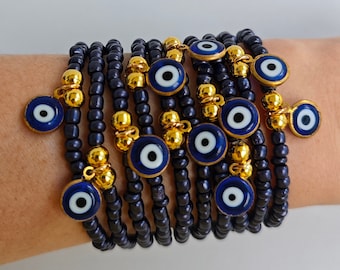 May include: A stack of blue and gold beaded bracelets with evil eye charms. Each bracelet has a small blue evil eye charm hanging from it.