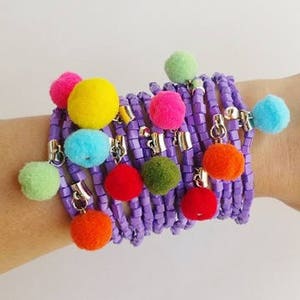 Pode incluir: Um bracelete de contas roxas com pompons coloridos pendurados.