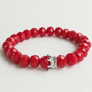 Könnte beinhalten: Rotes Perlenarmband mit einem silbernen Kronenanhänger.