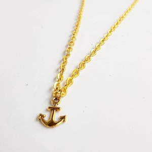 Pode incluir: Um colar de corrente de ouro com um pequeno pingente de âncora de ouro.