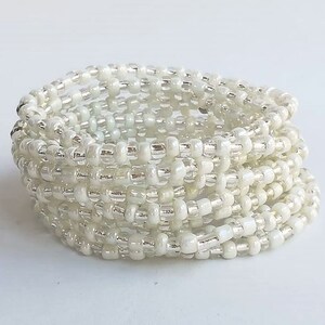 May include: A white beaded bracelet with silver accents. The bracelet is made of many small beads that are wrapped around each other to create a thick, layered look.