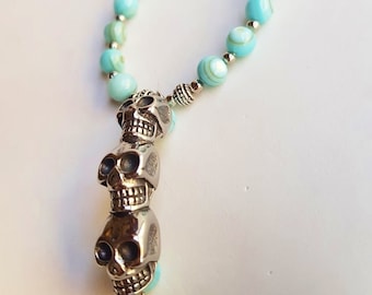 May include: A turquoise beaded necklace with a silver pendant featuring three stacked skull charms.