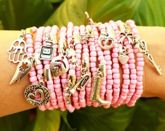 May include: A stack of pink beaded bracelets with various silver charms, including a heart, a key, a boot, a leaf, a perfume bottle, a butterfly, a hand, a wing, and a trumpet.