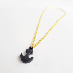 Pode incluir: Um colar de corrente dourada com um pingente de âncora preto.