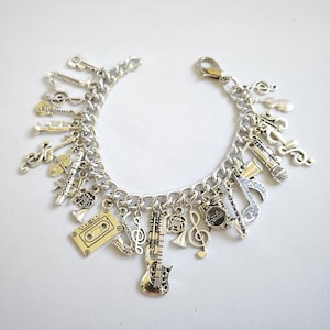 May include: A silver charm bracelet with a variety of music-themed charms, including a guitar, a violin, a trumpet, a saxophone, a music note, and a cassette tape.