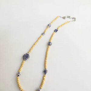 May include: A yellow wooden beaded necklace with blue and white porcelain charms. The charms feature geometric designs and floral patterns.
