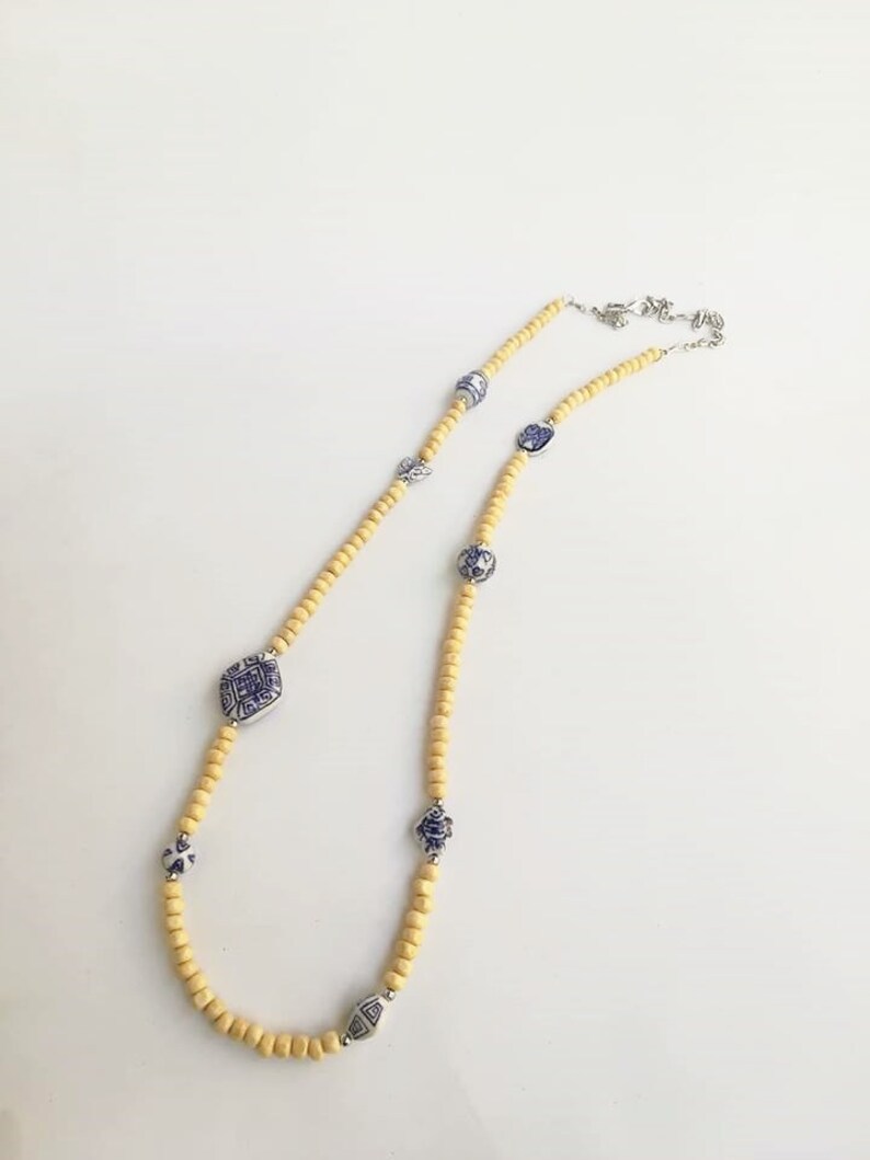 May include: A yellow wooden beaded necklace with blue and white porcelain charms. The charms feature geometric designs and floral patterns.