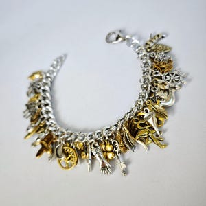 May include: A silver charm bracelet with a variety of gold and silver charms, including a ship's wheel, a key, a feather, a hand, a tree, and a crescent moon.