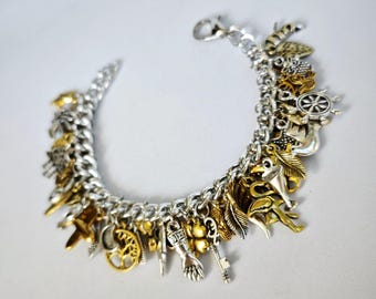 May include: A silver charm bracelet with a variety of gold and silver charms, including a ship's wheel, a key, a feather, a hand, a tree, and a crescent moon.
