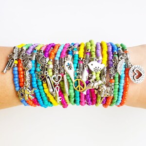 May include: A stack of colorful beaded bracelets with various silver charms, including a peace sign, a bird, a heart, and a key.