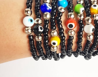 May include: A set of black beaded bracelets with colorful evil eye charms. The bracelets are stacked on a person's wrist.