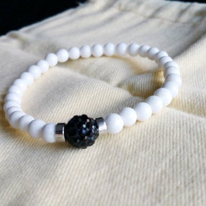 Op de afbeelding: Witte kralen armband met een zwart strass steentje in het midden.